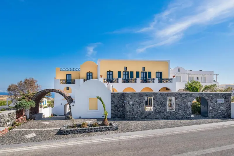 Bâtiment blanc aux fenêtres bleues et arches en pierre, sur une île ensoleillée.