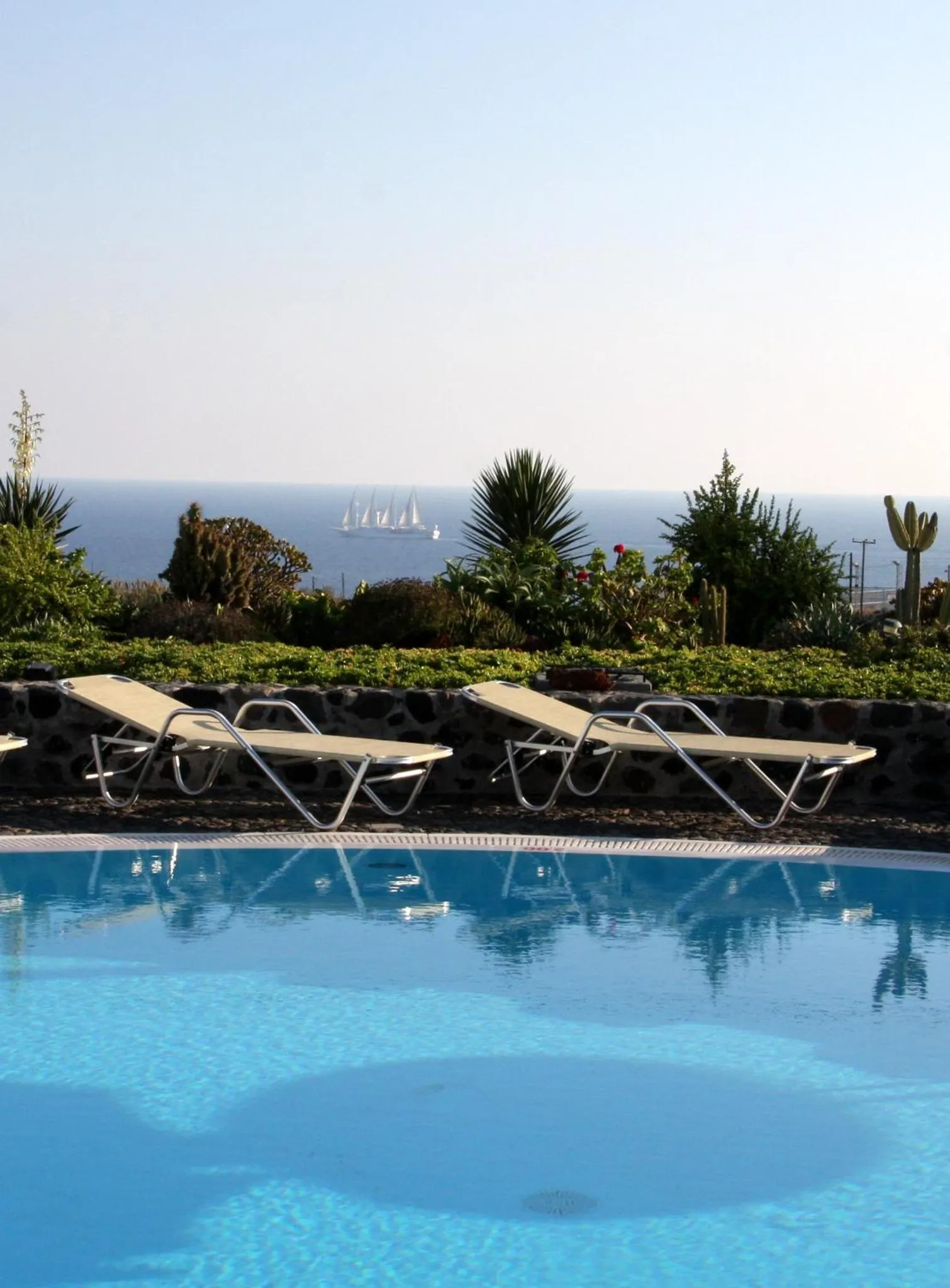 Transats blancs alignés au bord d'une piscine turquoise avec vue sur la mer.