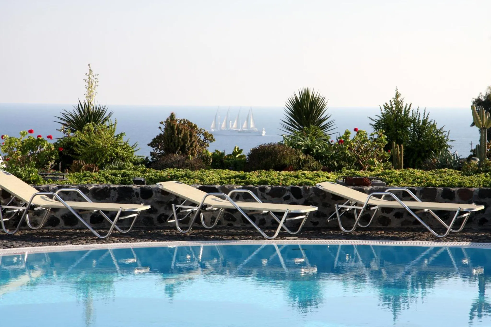 Transats blancs alignés au bord d'une piscine turquoise avec vue sur la mer.