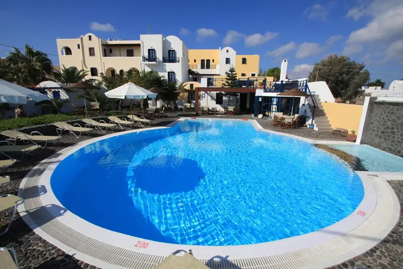 Piscine circulaire entourée de transats dans un complexe hôtelier blanc et bleu.