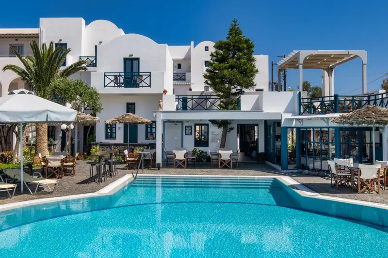 Bâtiment blanc à deux étages avec une piscine au premier plan et des parasols.
