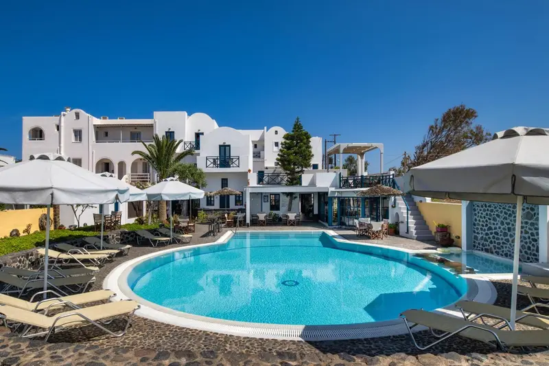 Bâtiment blanc avec piscine et parasols sous un ciel bleu.