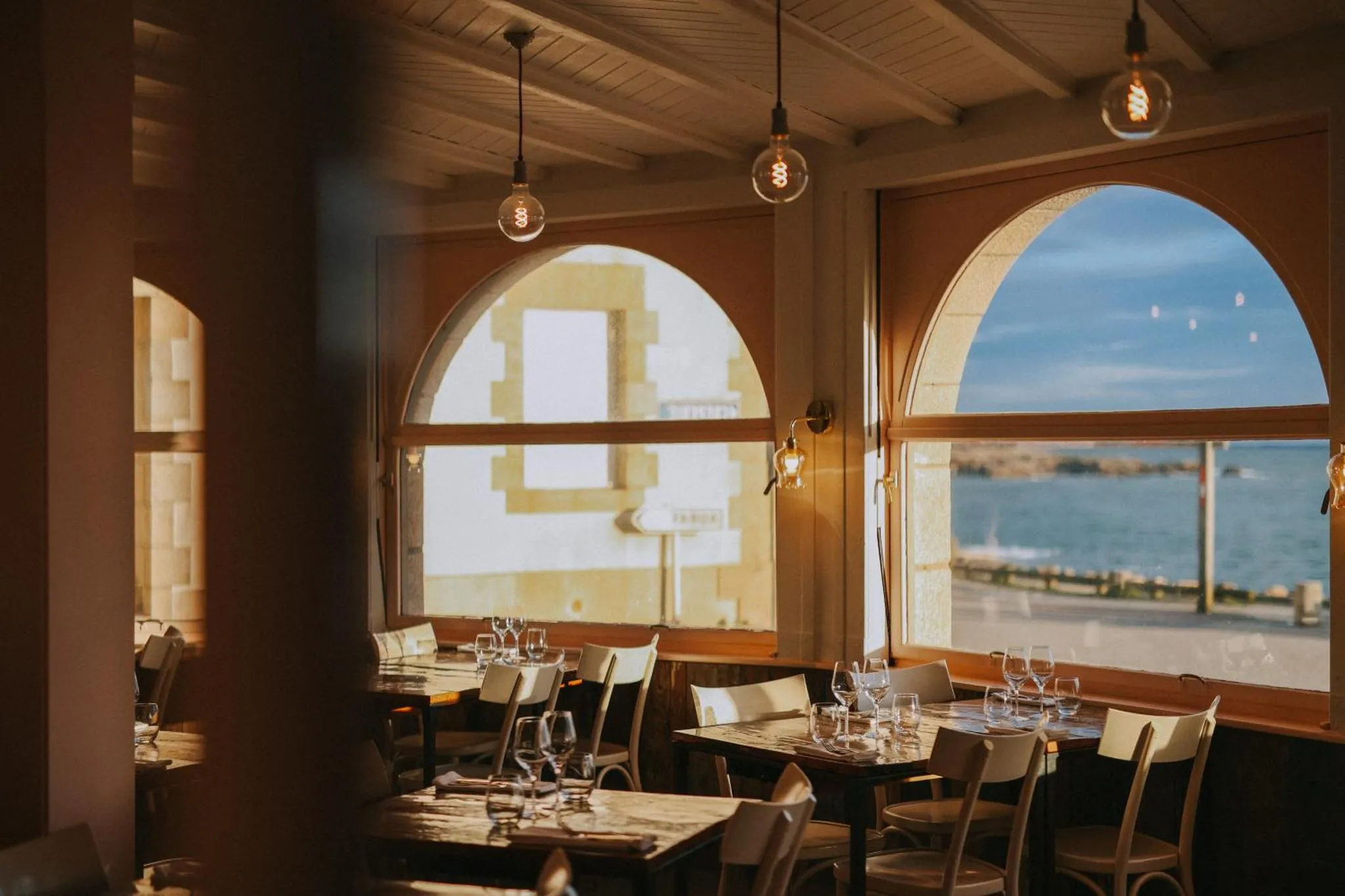 Une salle lumineuse avec des tables dressées face à une vue sur la mer.