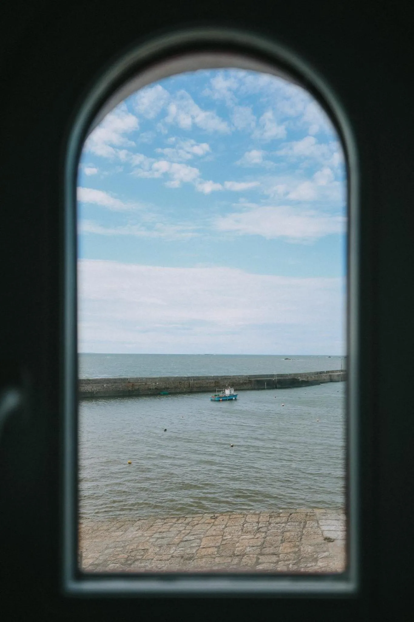 Vue sur la mer et un port depuis une fenêtre cintrée.