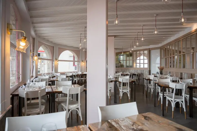 Une salle lumineuse avec des tables et des chaises blanches est décorée de luminaires suspendus.