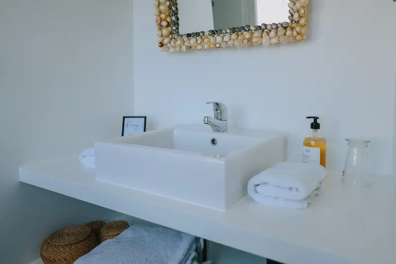 Un lavabo blanc et un miroir décoré de coquillages dans une salle de bain lumineuse.