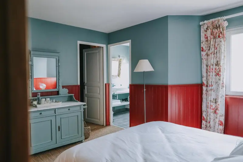Une chambre lumineuse aux murs bleus et rouges, avec un lit et une commode.