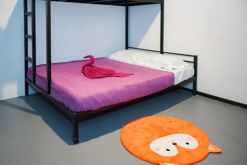 Lit superposé avec draps violets et décoration en forme de chat sur le sol.