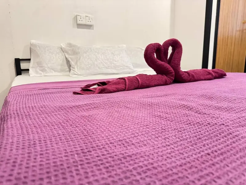 Un lit recouvert d'une couverture mauve est orné de serviettes enroulées en forme de cœur.