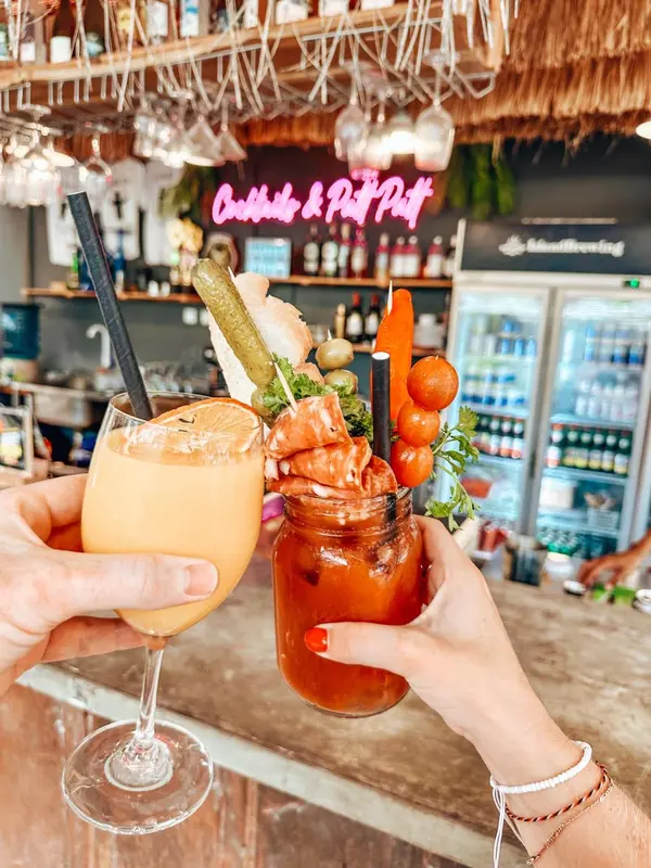 Deux verres garnis de fruits de mer et de légumes sont levés dans un bar lumineux.