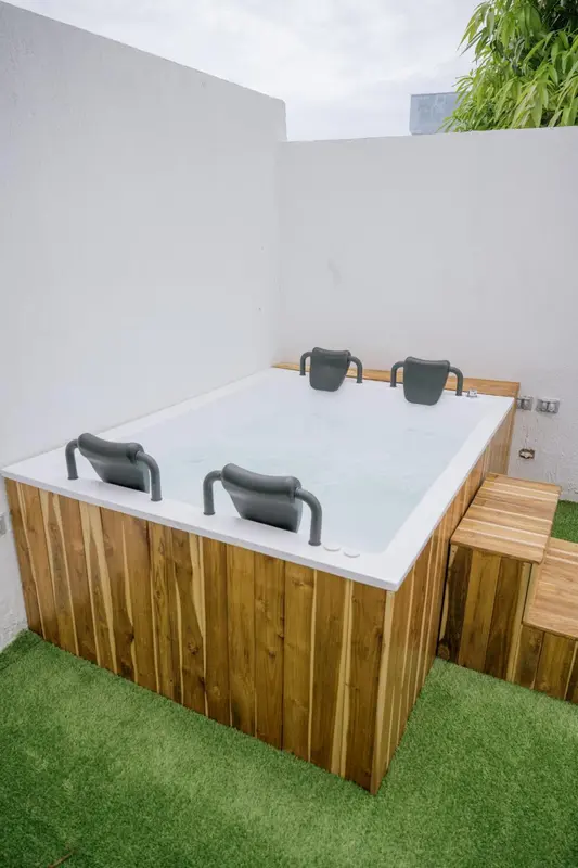Un jacuzzi en bois est installé sur une terrasse avec gazon synthétique.