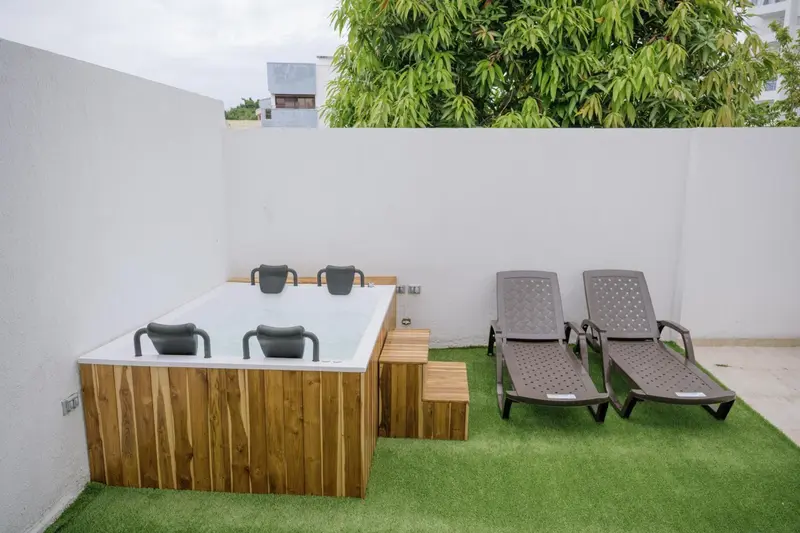 Un espace extérieur aménagé avec un jacuzzi et des chaises longues sur une pelouse artificielle.