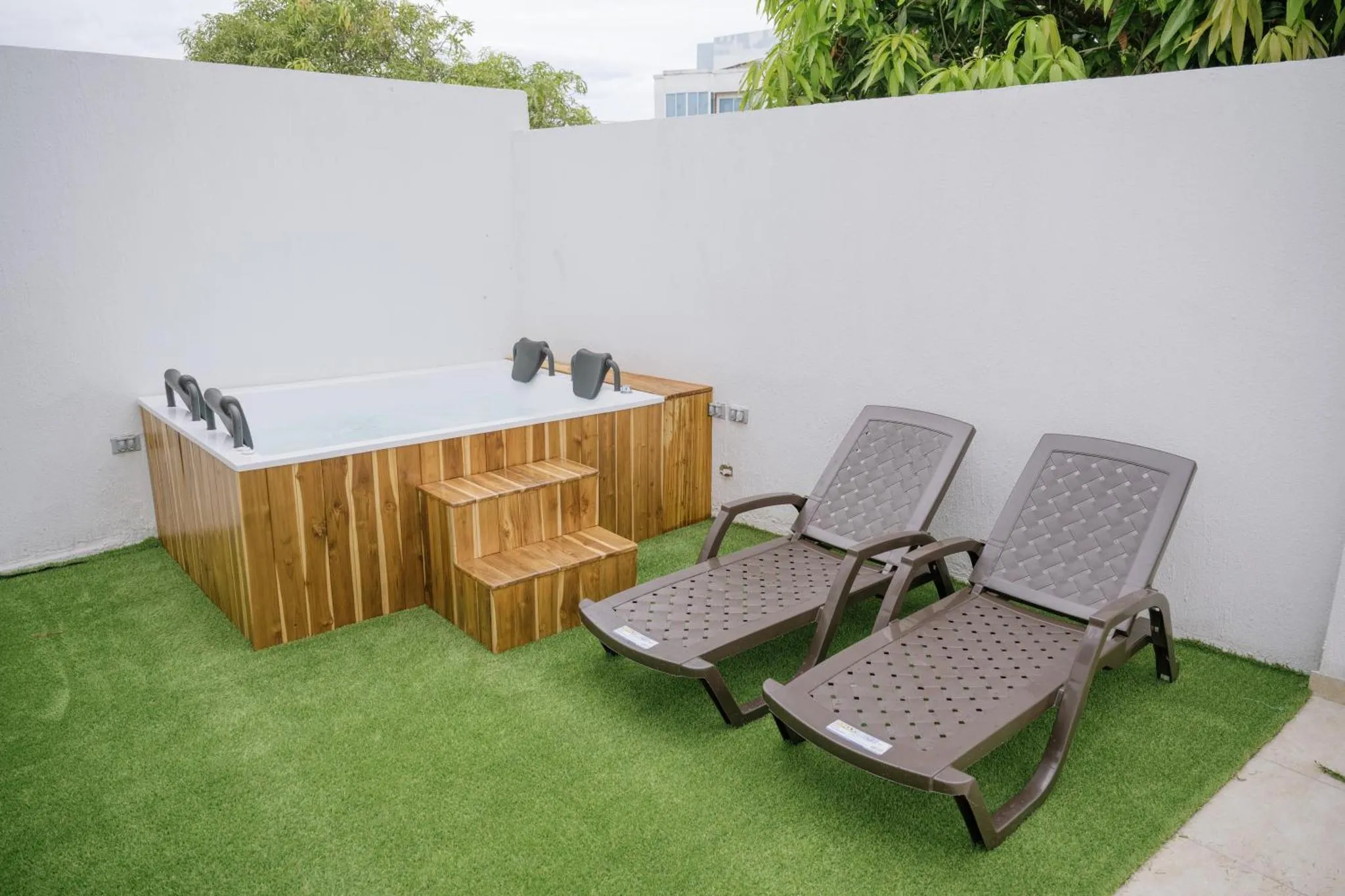 Deux transats sont placés devant un jacuzzi extérieur sur une pelouse artificielle.