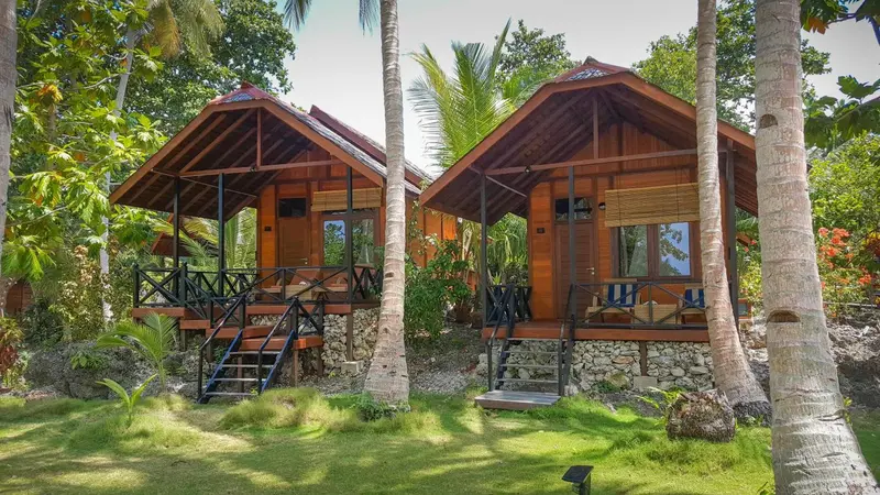 Deux bungalows en bois sur pilotis au milieu d'une végétation tropicale.