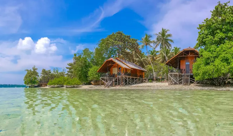 Cabanes en bois sur pilotis au bord d'une eau turquoise et d'une plage de sable blanc.