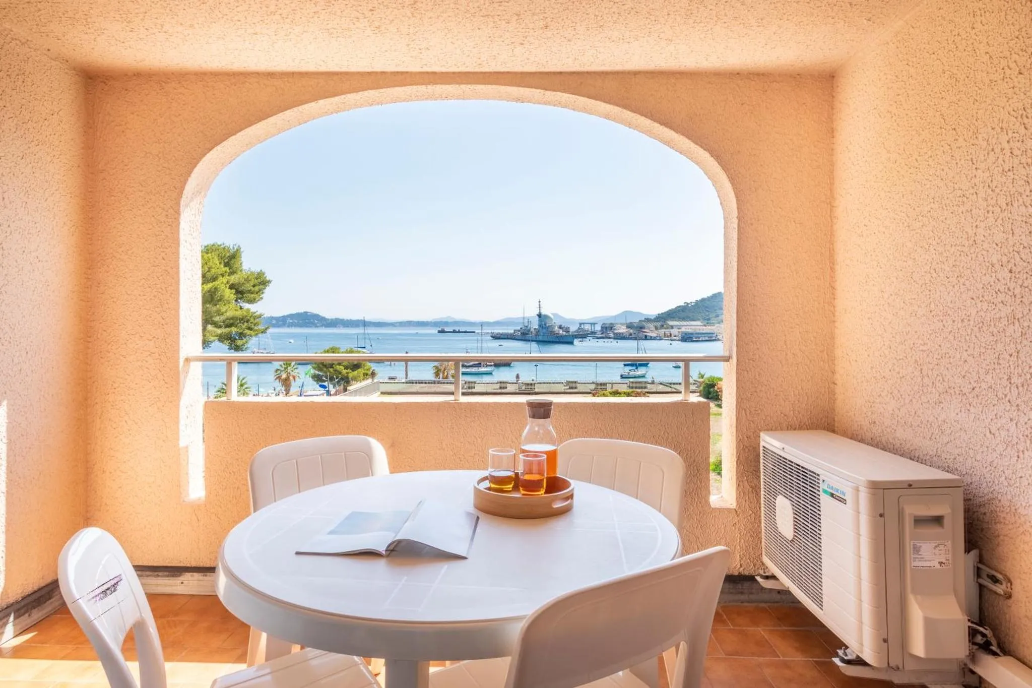 Une table ronde avec des verres et un livre sur un balcon donnant sur la mer.