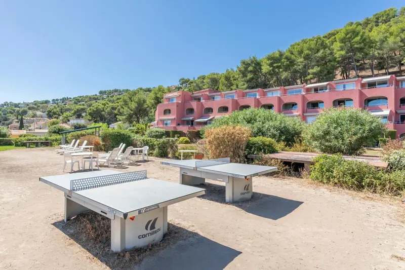 Tables de ping-pong sur une terrasse ensoleillée devant un bâtiment rose.