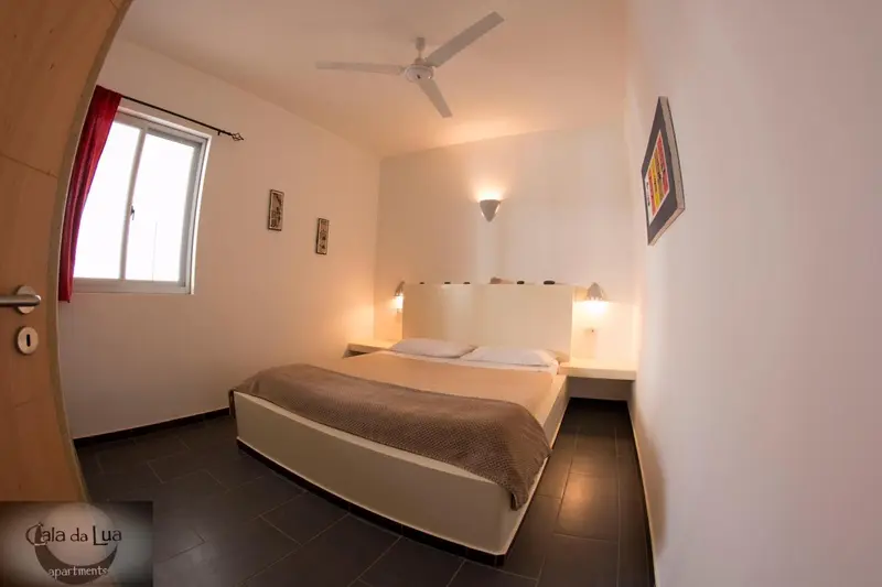 Une chambre lumineuse avec un grand lit et un ventilateur au plafond.