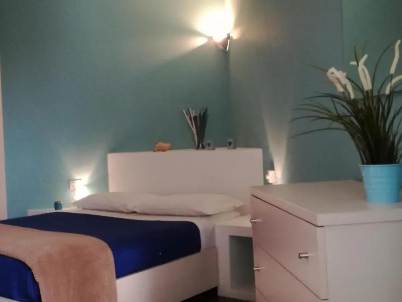 Une chambre lumineuse avec un lit recouvert d'une couverture bleue et d'un plaid beige.