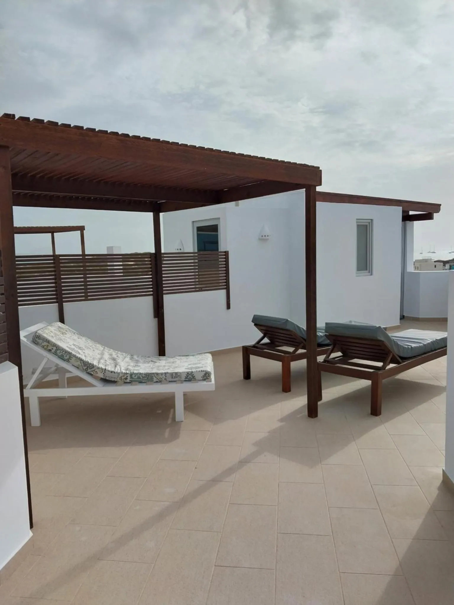 Deux transats blancs sont placés sur une terrasse carrelée ombragée.