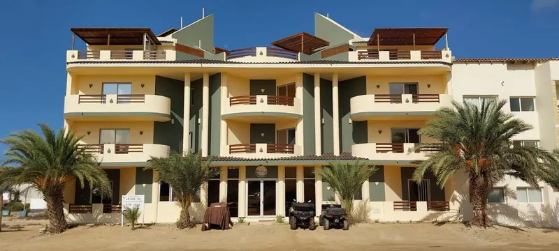 Bâtiment jaune et vert avec des balcons et des palmiers devant.