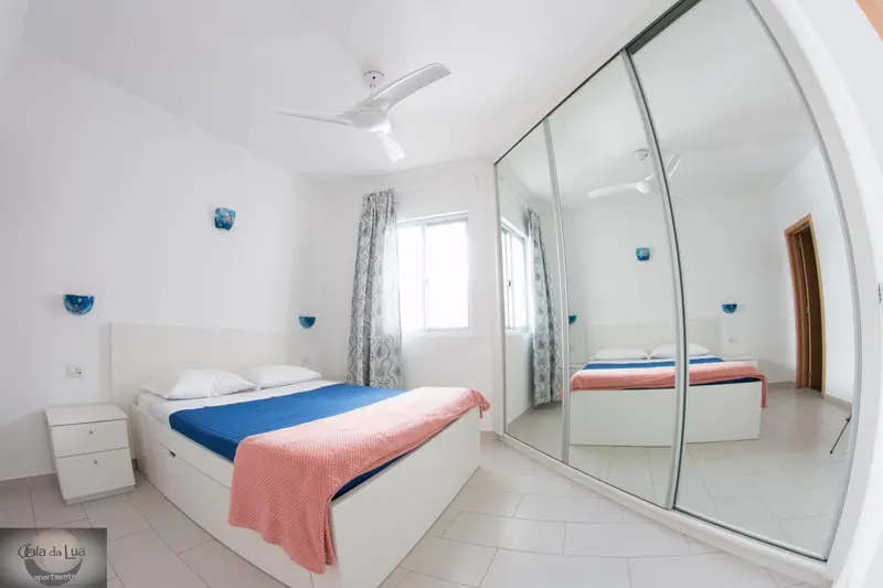 Chambre lumineuse avec un grand lit et des armoires miroir.