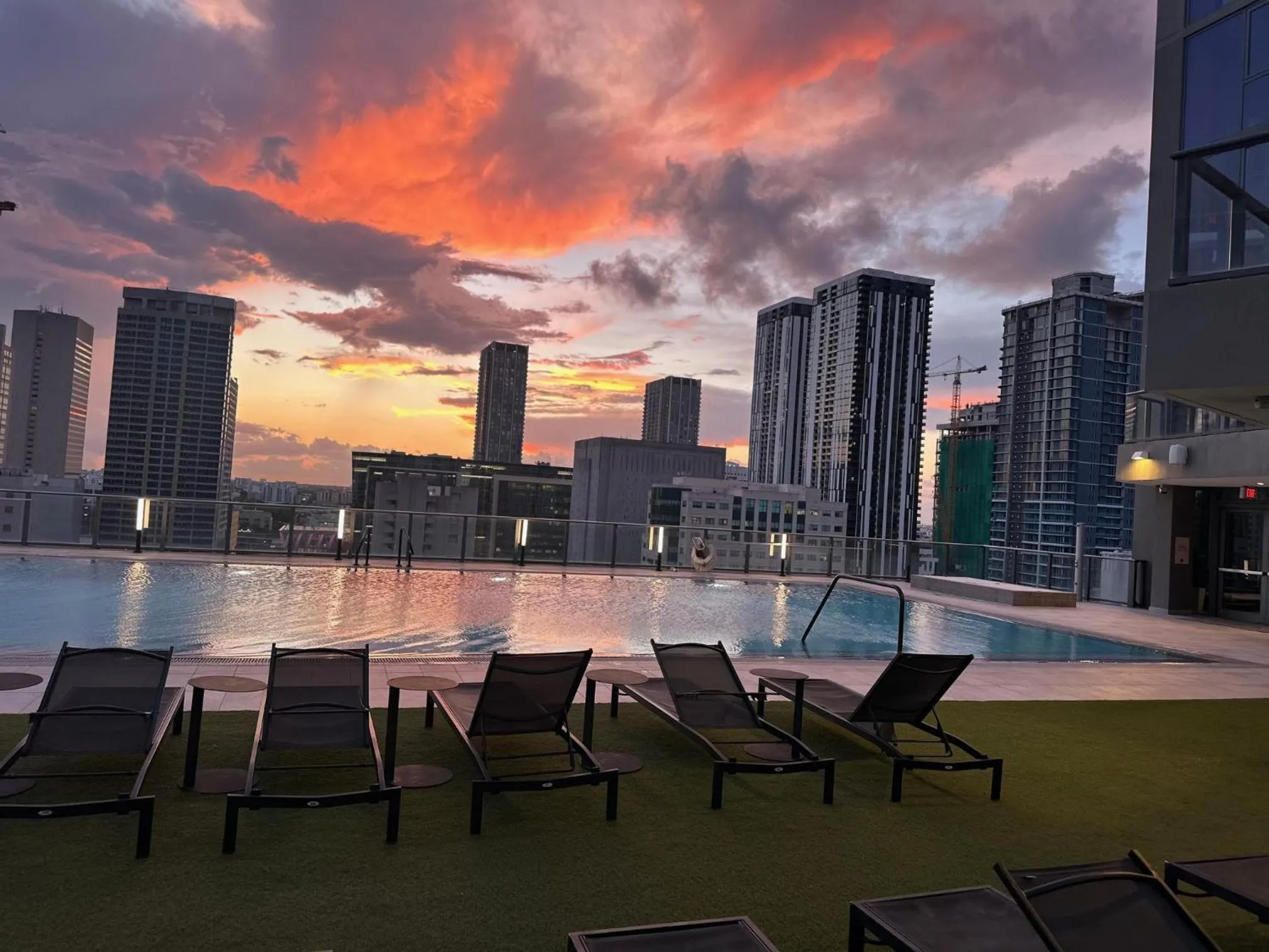 Transats alignés au bord d'une piscine avec vue sur une ville au coucher du soleil.