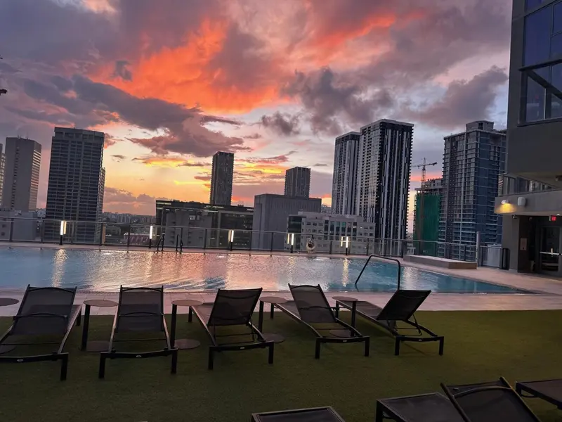 Transats alignés au bord d'une piscine avec vue sur une ville au coucher du soleil.