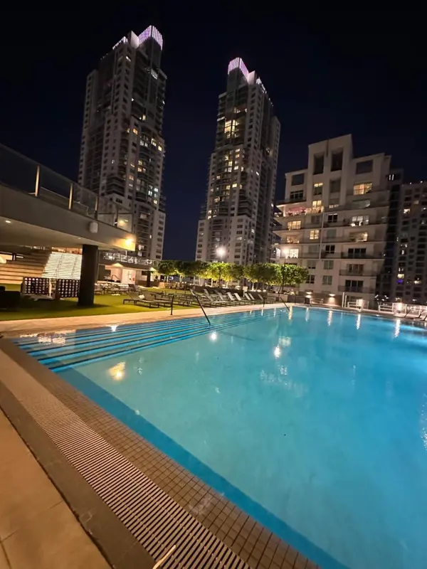 Une piscine illuminée au premier plan, avec des bâtiments modernes en arrière-plan.