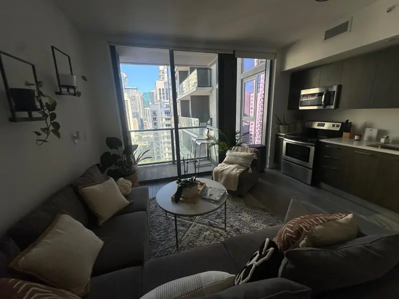 Un espace de vie moderne avec canapé, table basse et cuisine ouverte donnant sur une vue urbaine.