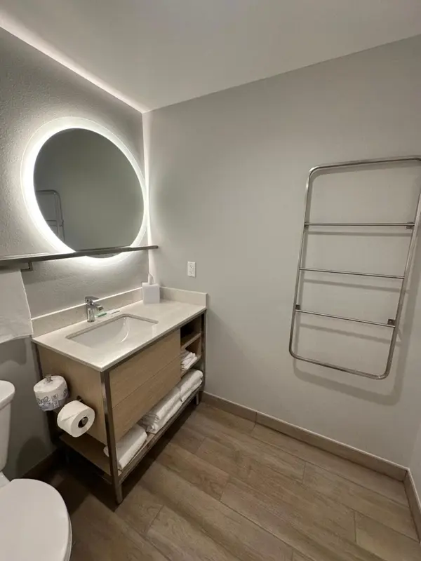 Une salle de bain claire avec un grand miroir rond et un meuble vasque.