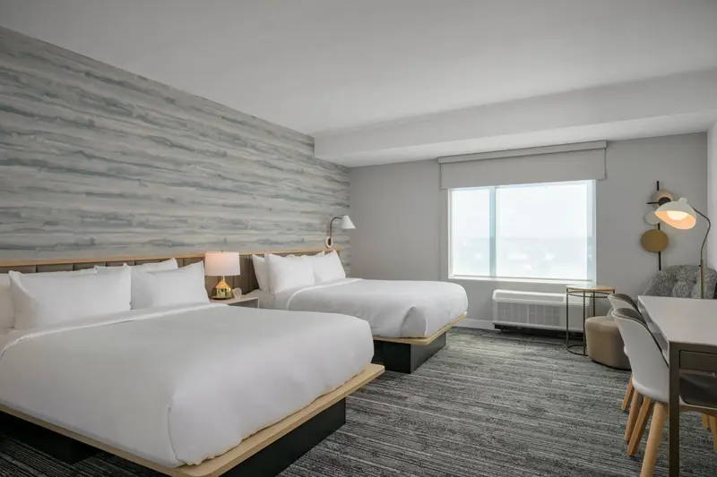 Une chambre d'hôtel lumineuse avec deux lits et un bureau près de la fenêtre.