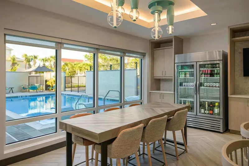 Une salle lumineuse avec une grande baie vitrée donnant sur une piscine et une table à manger en bois.