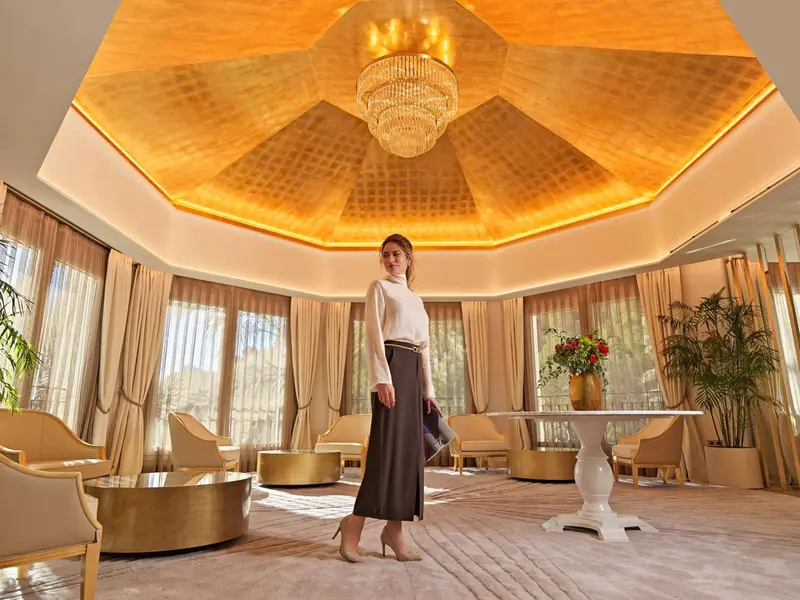 Une femme se tient dans un espace intérieur lumineux avec un plafond doré et des meubles élégants.