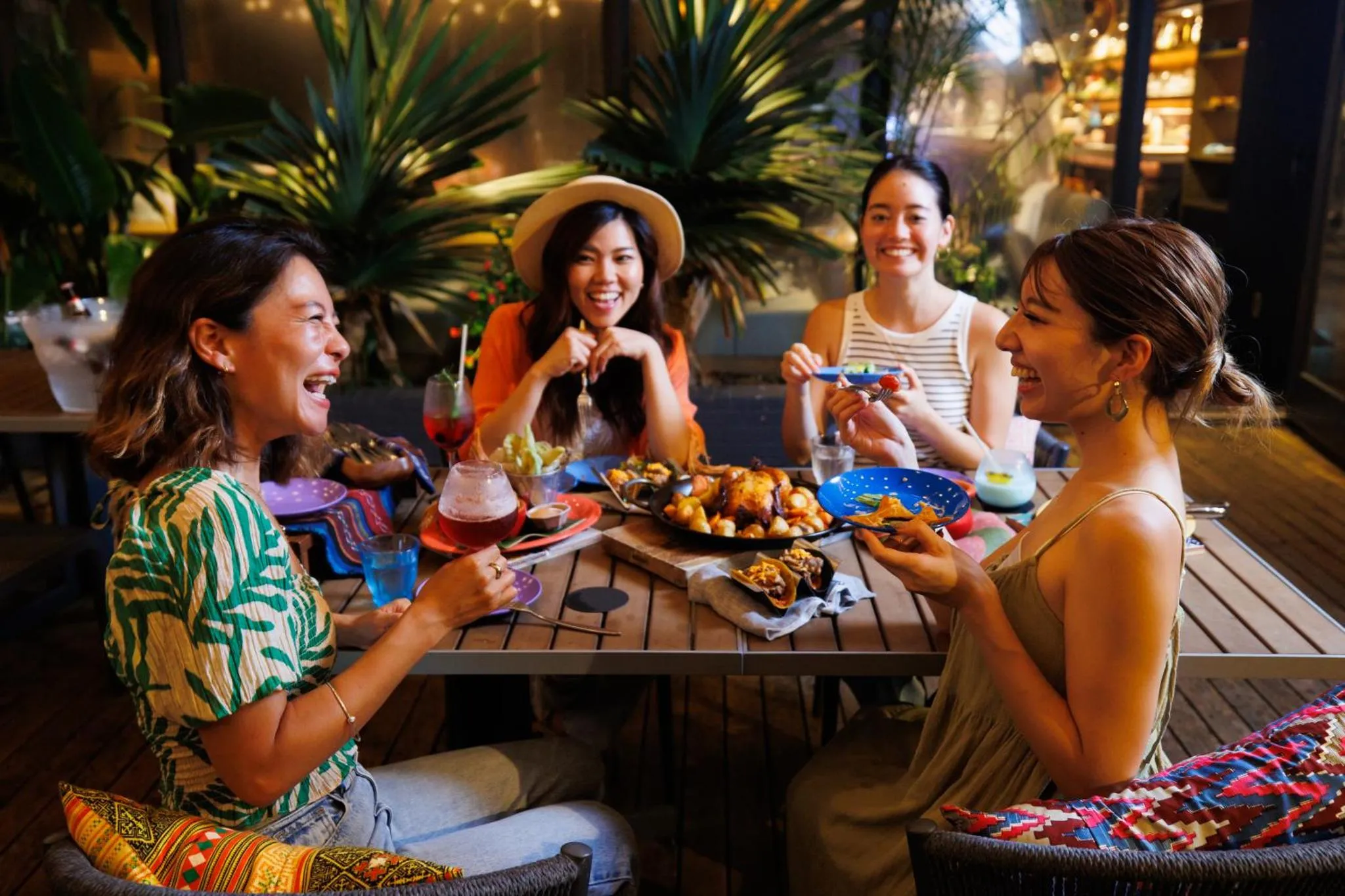 Quatre femmes sourient et discutent autour d'une table garnie de plats et de boissons.
