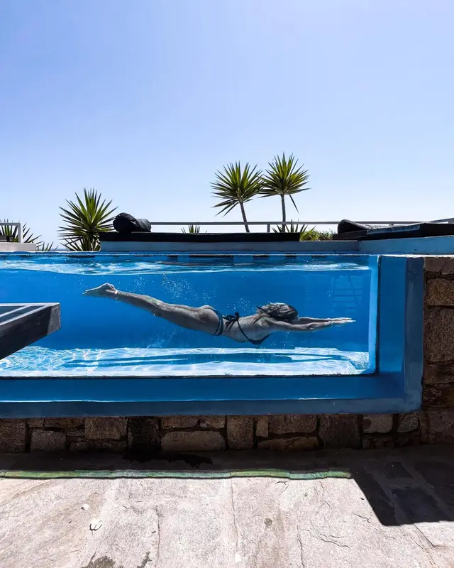 Une personne nage dans une piscine à débordement avec vue sur la mer et la végétation.