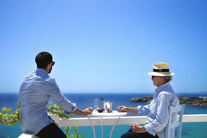 Deux hommes sont assis à une table en extérieur avec vue sur la mer.