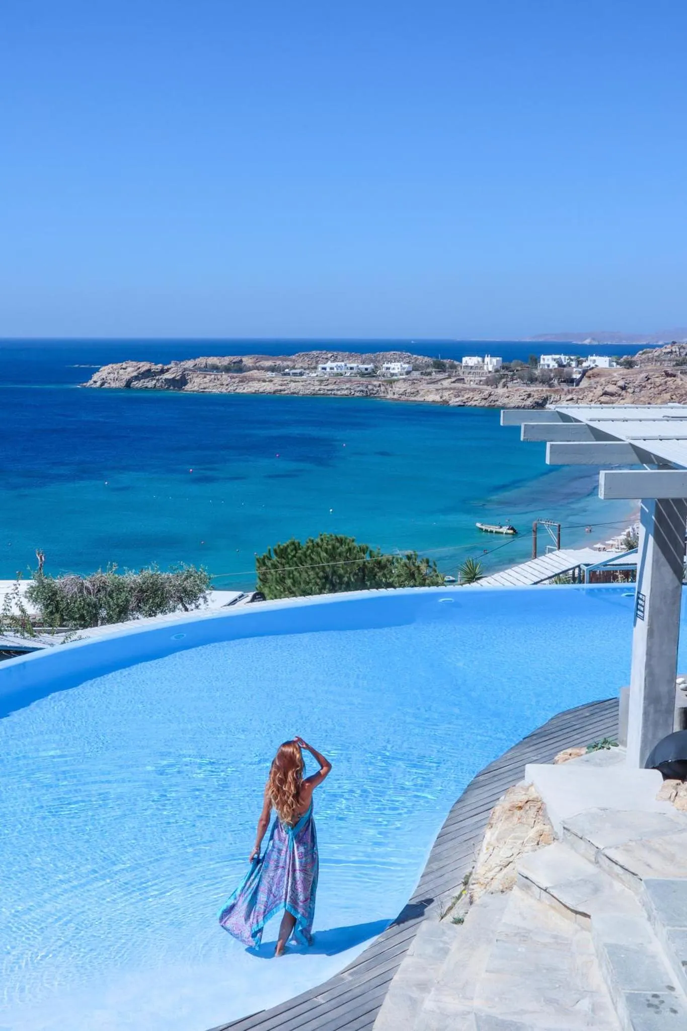 Une femme se tient au bord d'une piscine à débordement avec vue sur la mer.