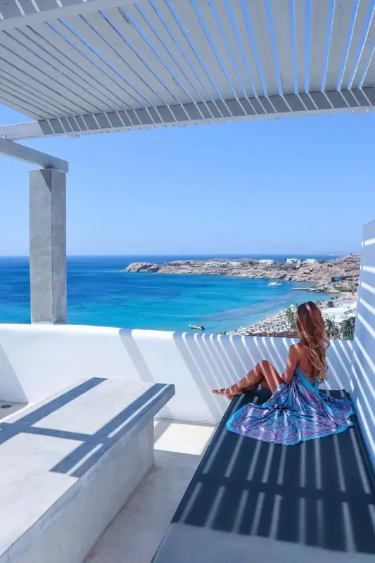 Une femme assise sur une terrasse surplombe une plage et la mer.