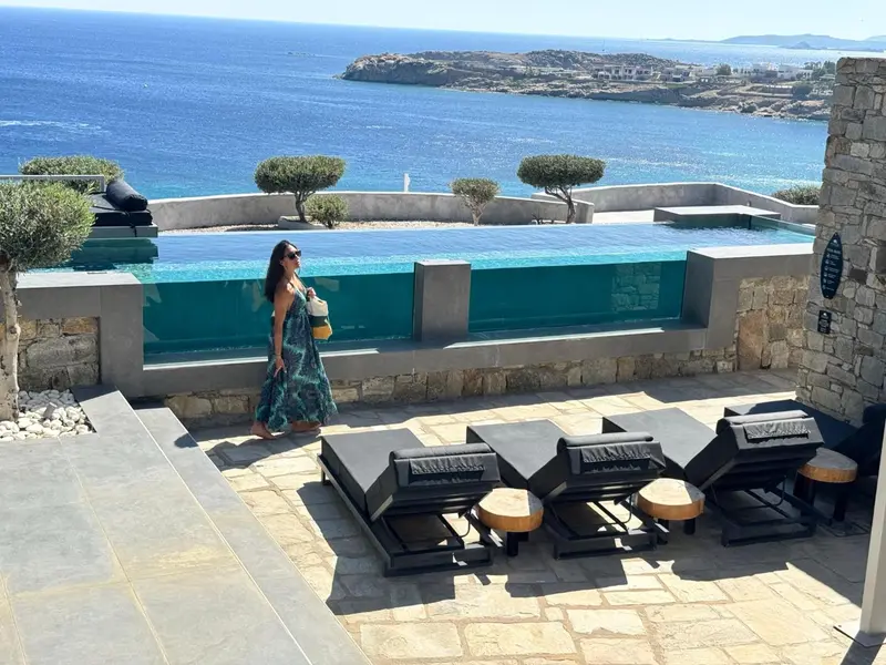 Une femme se tient près d'une piscine à débordement avec vue sur la mer.