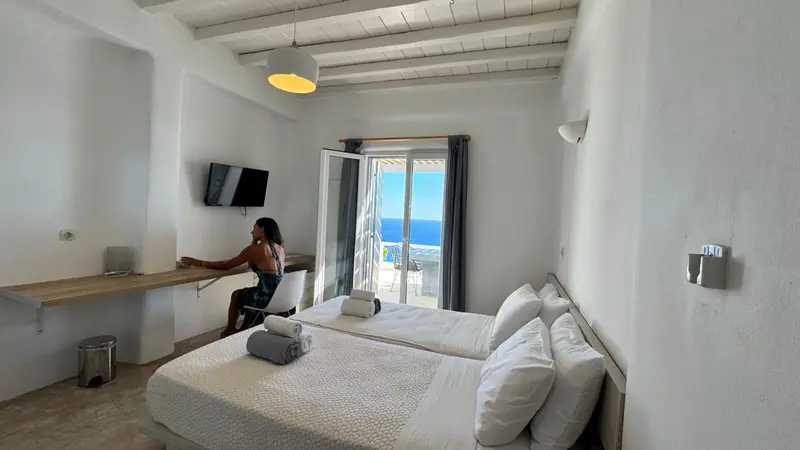 Une chambre lumineuse avec un bureau et un lit fait face à une vue sur la mer.