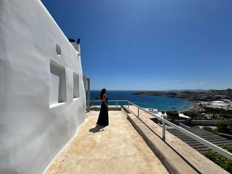 Une femme contemple la vue depuis une terrasse ensoleillée.