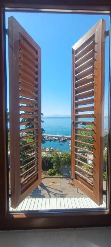 Vue sur la mer depuis une fenêtre ouverte avec des volets en bois.