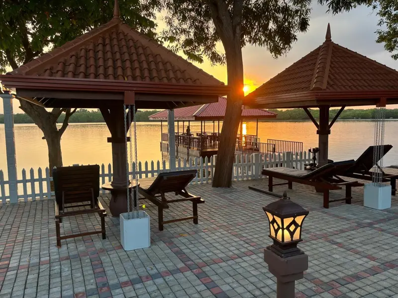 Deux pavillons de bois sur une terrasse au bord de l'eau au coucher du soleil.
