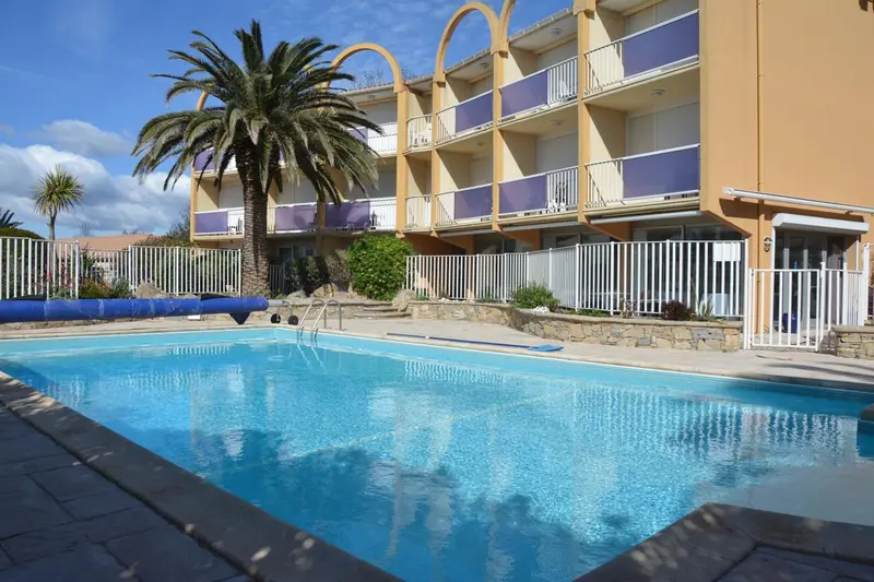 Piscine turquoise devant un bâtiment aux balcons colorés et une végétation luxuriante.