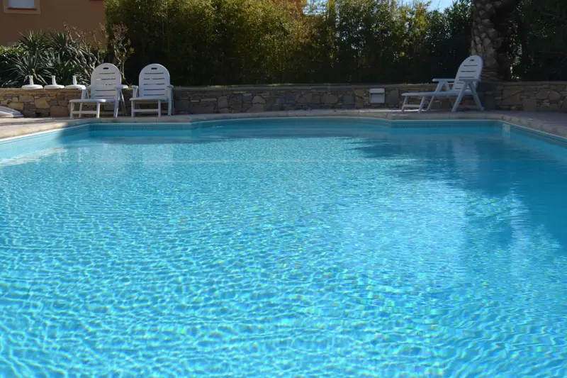 Une piscine rectangulaire aux eaux turquoise reflète le ciel bleu.
