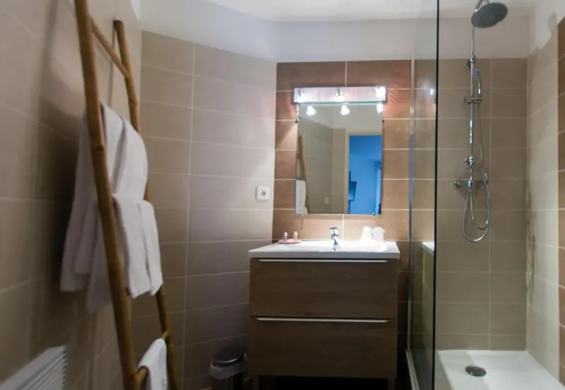Une salle de bain moderne avec douche à l'italienne et serviettes sur un porte-serviettes en bambou.