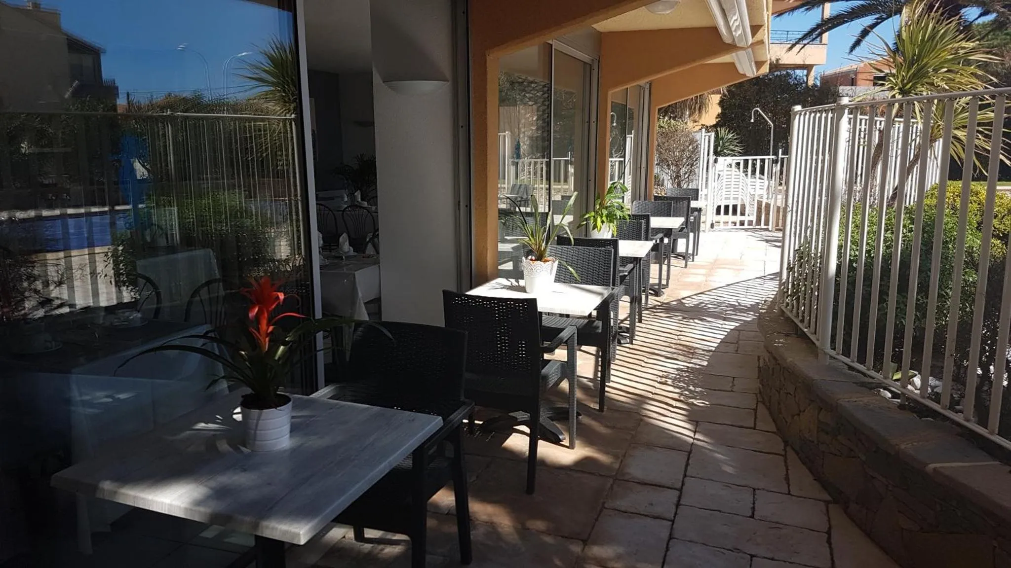 Terrasse ombragée avec tables et chaises près d'une piscine.