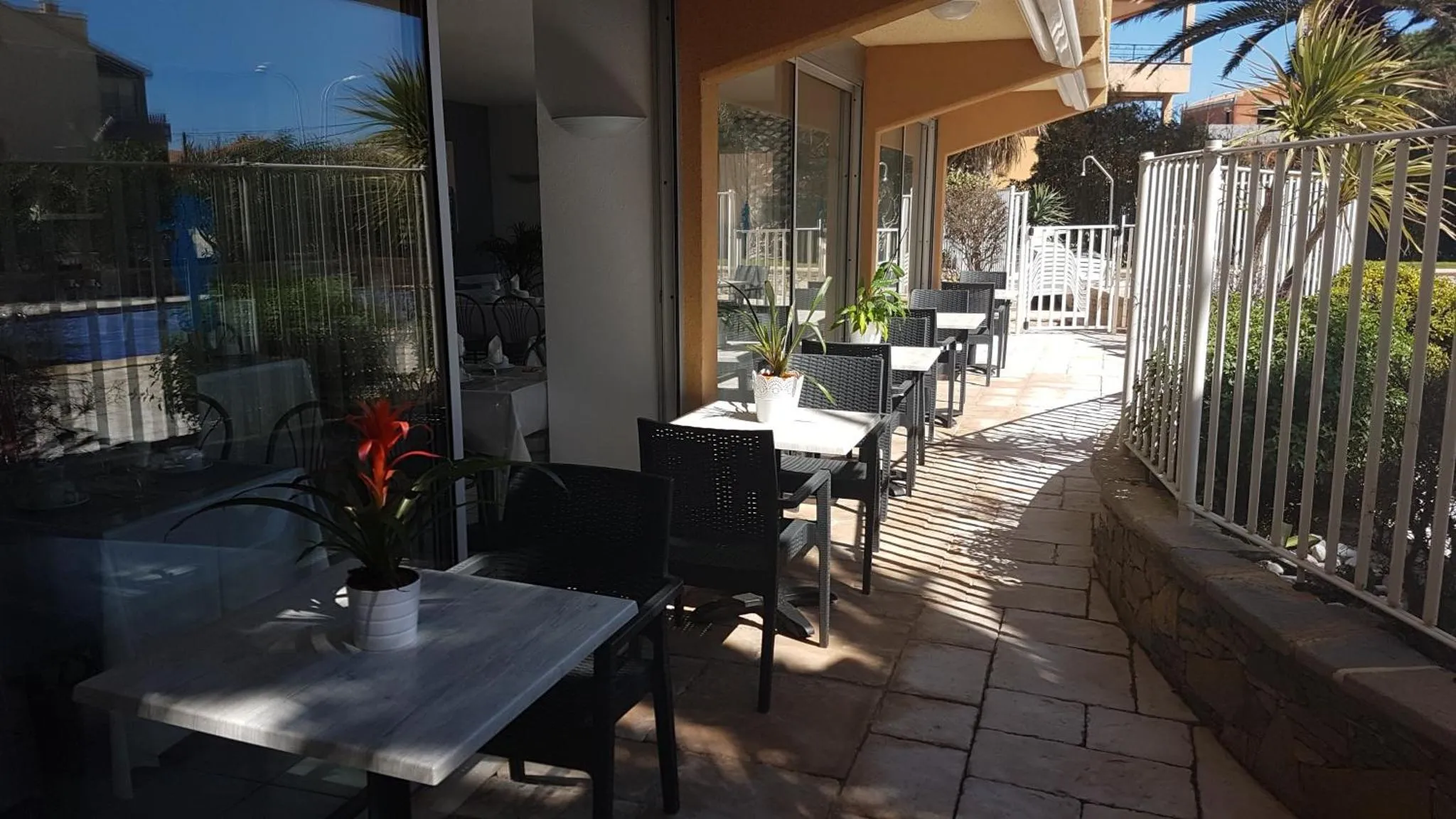 Terrasse ombragée avec tables et chaises près d'une piscine.