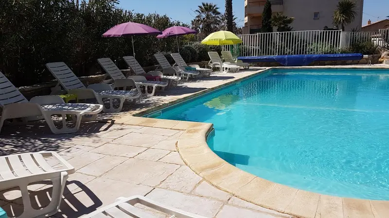 Transats blancs alignés au bord d'une piscine turquoise sous le soleil.